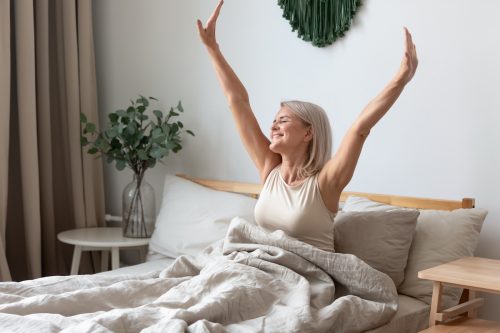A mature woman looking happy and stretching in bed.