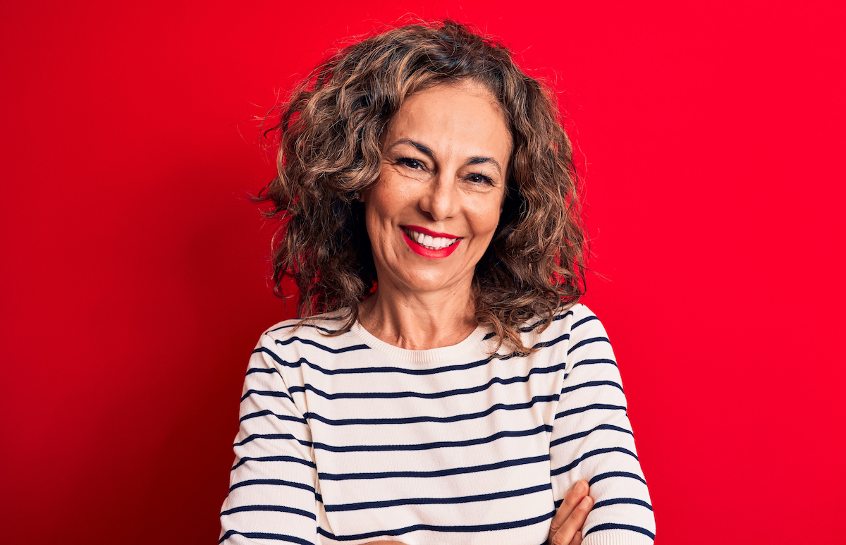 A middle-aged brunette woman smiling and wearing a black-and-white striped shirt against a red background.