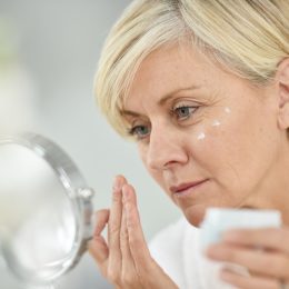 Senior woman in bathroom applying anti-aging lotion