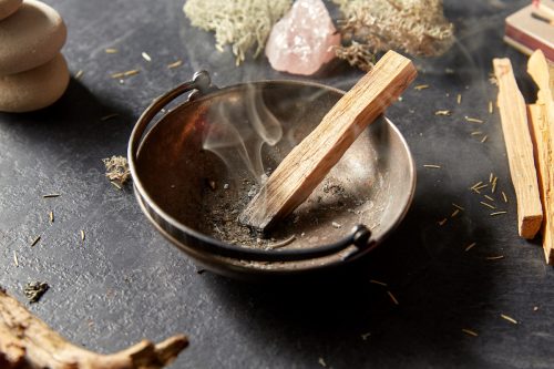 Palo Santo sticks burning in a bowl surrounded by crystals