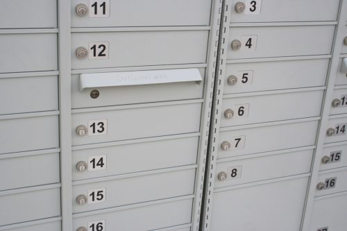 A shot of some new mailboxes in a neighborhood. The boxes are letter size and numbered. One box is for outgoing mail.