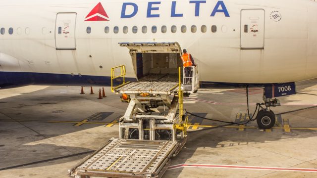 ground crew member on a special loading platform opens the side cargo bay door of a Delta Airlines passenger airplane.