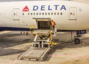 nhân viên mặt đất trên một bệ chất hàng đặc biệt mở cửa khoang chứa hàng bên của một chiếc máy bay chở khách của Delta Airlines.