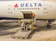 ground crew member on a special loading platform opens the side cargo bay door of a Delta Airlines passenger airplane.