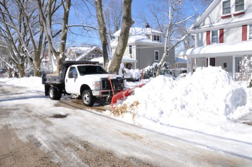 Plow truck clearing snow on suburban street.