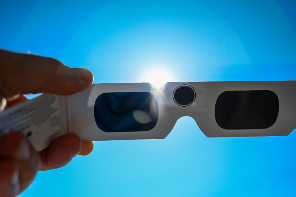 A closeup of a pair of solar eclipse viewing glasses being held up to the sun