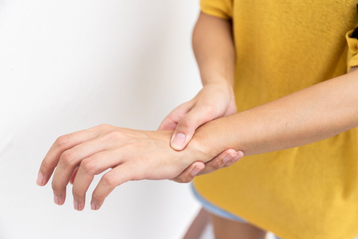 Woman in yellow clothes using hand to hold wrist with feeling pain, suffer, hurt and tingling. Concept of Guillain barre syndrome and numb hands disease.