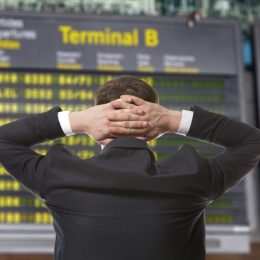 A man looking at an airline departure board with his hands behind his head