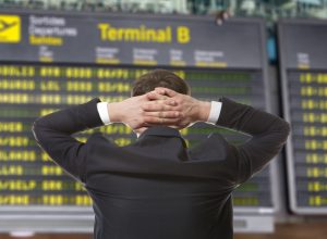 A man looking at an airline departure board with his hands behind his head
