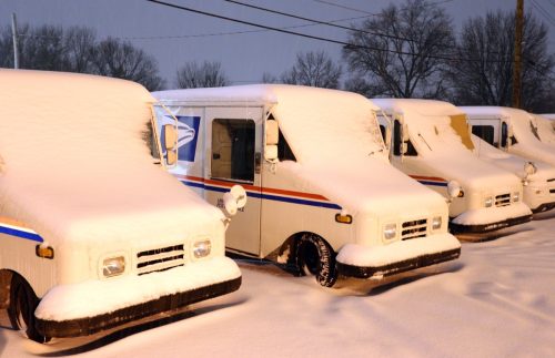 Postal delivery trucks are being buried in snow during a snowstorm in Olivette, Missouri. Olivette is a suburb of St. Louis, Missouri.
