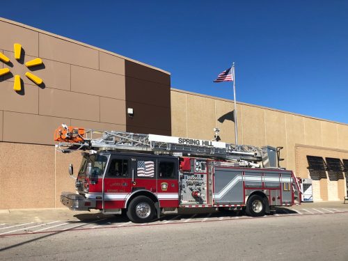A new large ladder-style fire truck in front of a Walmart with an American flag fluttering in the wind.
