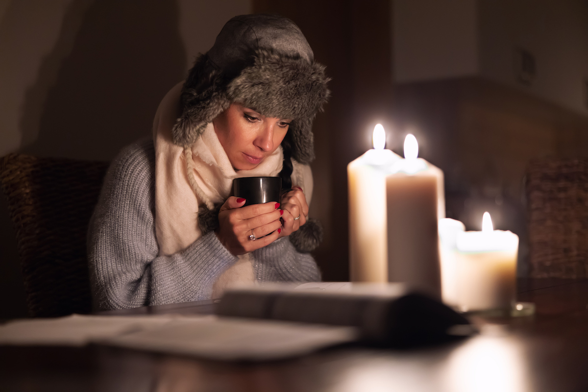 woman keeps warm by candlelight in a winter power outage