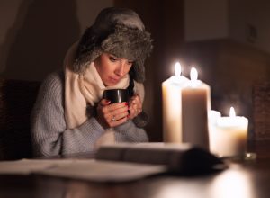 woman keeps warm by candlelight in a winter power outage