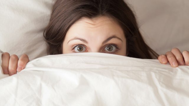 A young woman in bed with the covers pulled up over her face