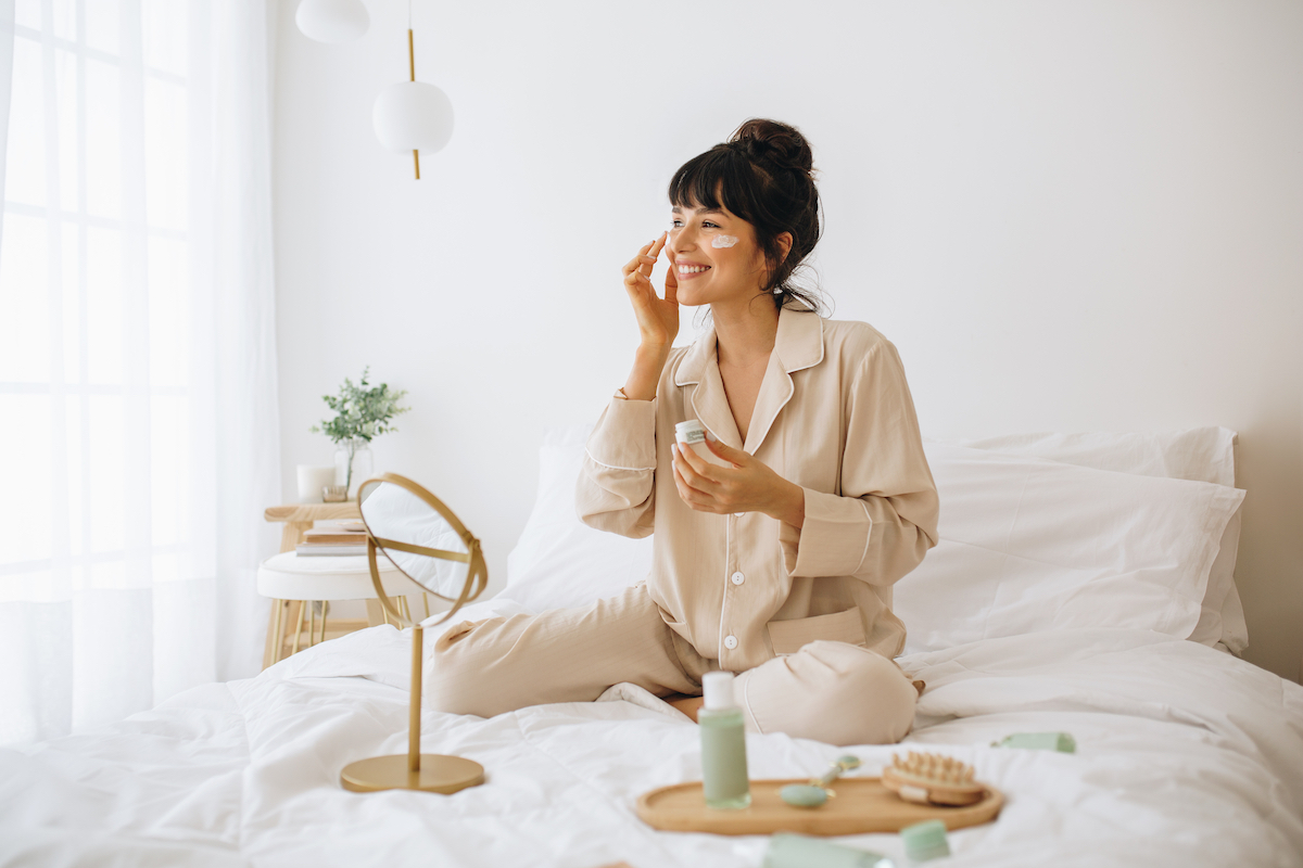Woman sitting on bed in pajamas doing skincare ritual