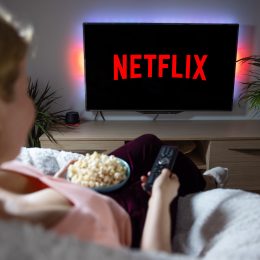 A woman sitting on a couch with popcorn watching Netflix on a TV