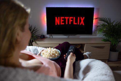 A woman sitting on a couch with popcorn watching Netflix on a TV