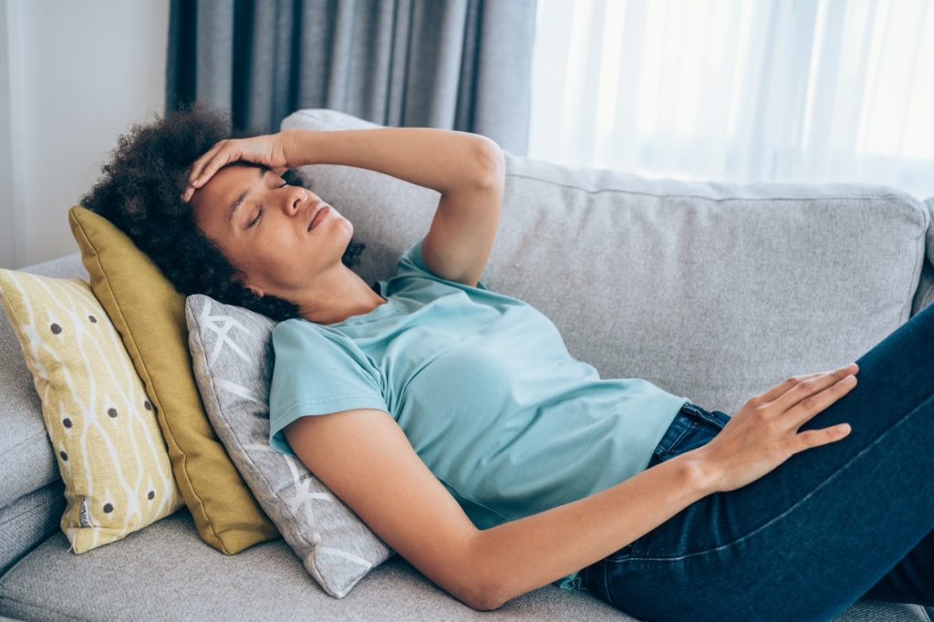 woman lying on the couch and holding her head with hand.