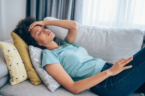 woman lying on the couch and holding her head with hand. Ill woman lying on the sofa with high temperature.