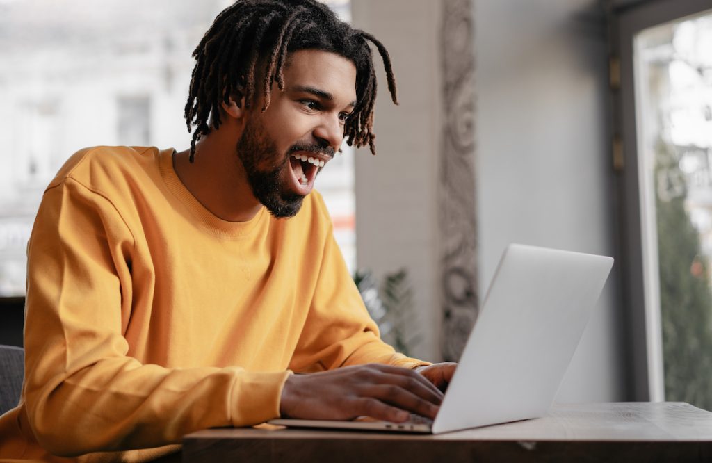 An excited young man in a yellow shirt on his laptop