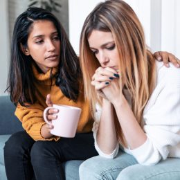 A young woman comforting her sad friend while sitting on the couch.