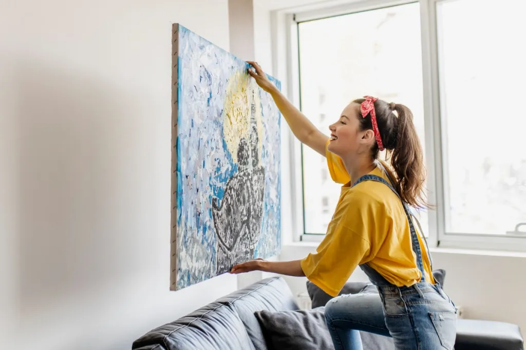 young woman hanging painting at home