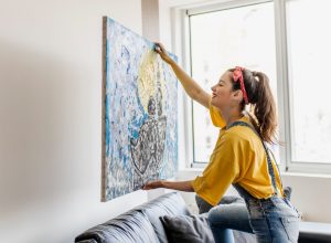 young woman hanging painting at home