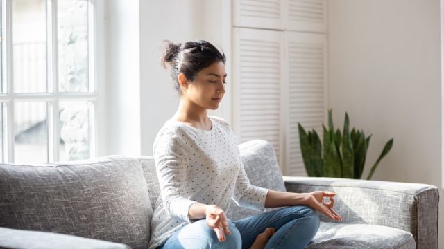 Indian female sitting on couch in lotus pose meditating