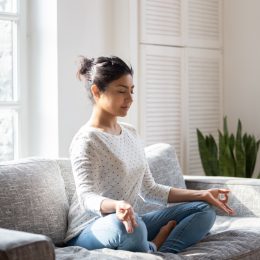 Indian female sitting on couch in lotus pose meditating