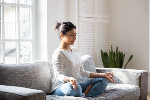 female sitting on couch in lotus pose meditating