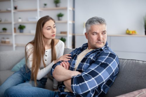 Annoyed man sitting on cough while his partner tries to comfort him