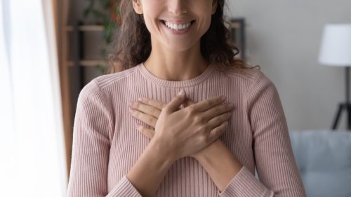 Woman smiling with her hands on her chest wearing a pink sweater.