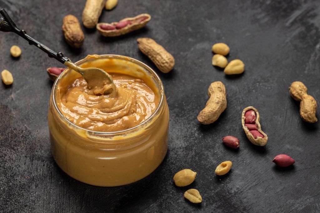 Open Jar of Peanut Butter on counter with peanuts strewn about
