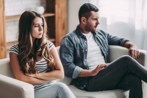 Unhappy Couple sitting on couch together frowning