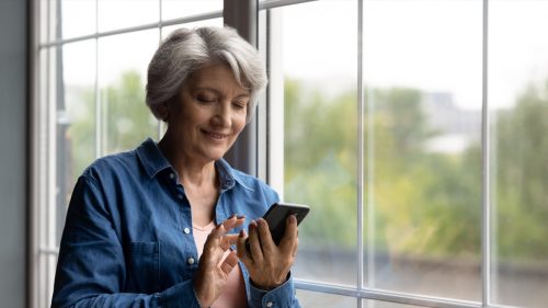 Woman smiling looking at her phone while standing next to a window
