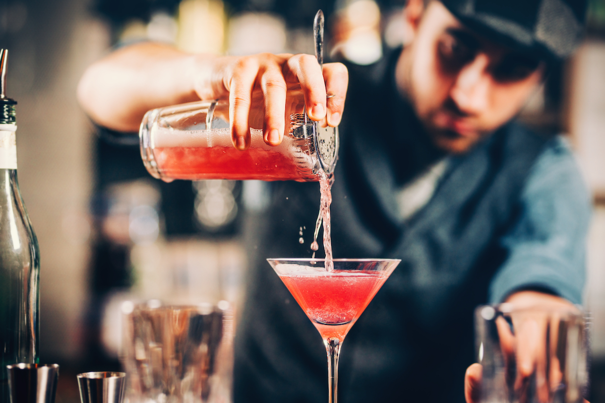 barman preparing and pouring red cocktail in martini class.