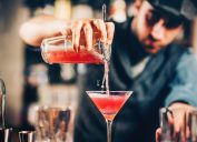 barman preparing and pouring red cocktail in martini class.