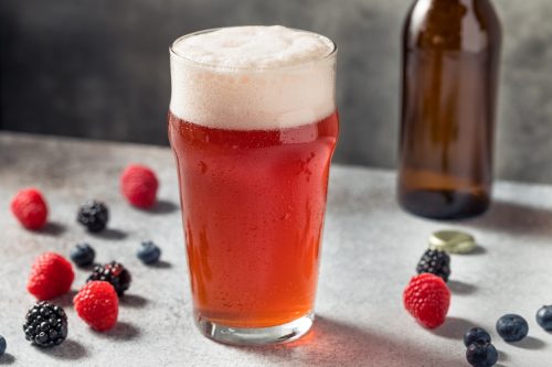 A berry beer shandy on a table surrounded by raspberries and blackberries.
