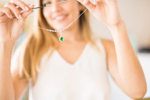 Close up of a woman holding up an emerald and diamond necklace