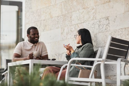 Portrait of two young people enjoying coffee in outdoor cafe, copy space