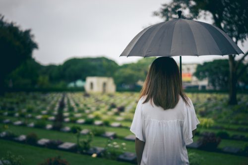 woman overlooking a graveyard while holding a black umbrella