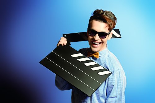 man in sunglasses holding a clapper board in front of blue background