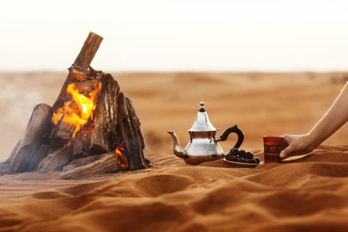 arabian dates, teapot, tea cup, and fire situated in the middle of the desert