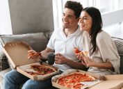 Cặp đôi hạnh phúc trên ghế sofa, mỗi người có một hộp bánh pizza trên đùi.