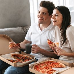 A happy couple on the couch, each with a pizza box on their laps.