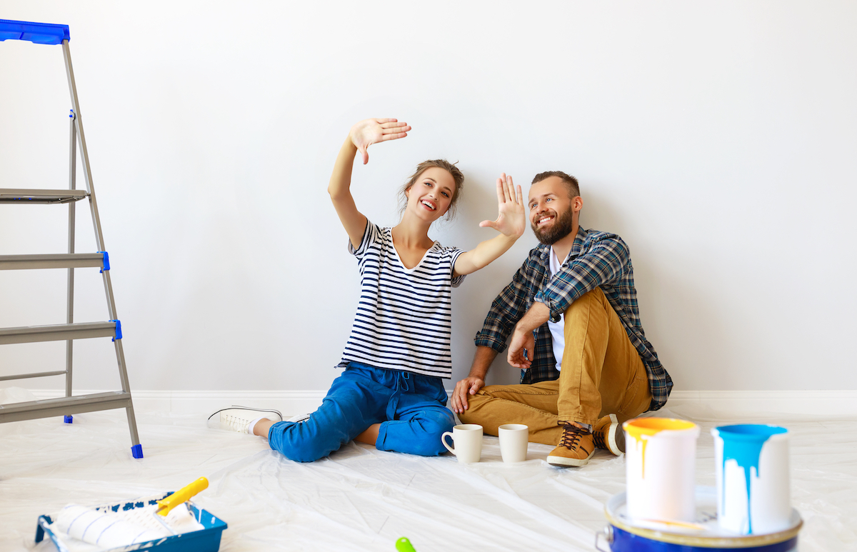 A young couple sits on the floor to take a break from painting a room