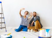 A young couple sits on the floor to take a break from painting a room