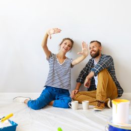 A young couple sits on the floor to take a break from painting a room