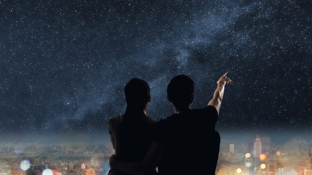 Silhouette of couple sit on ground point faraway on the roof above the city in the night.