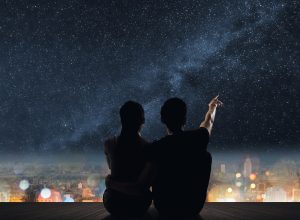 Silhouette of couple sit on ground point faraway on the roof above the city in the night.